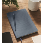Caderno de capa dura com caneta no interior, folhas A5 pautadas cor azul-marinho vista conjunto